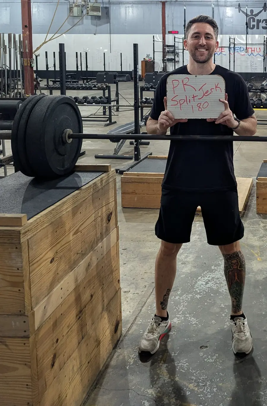 Josh smiling and holding a board that reads PR split jerk 180.