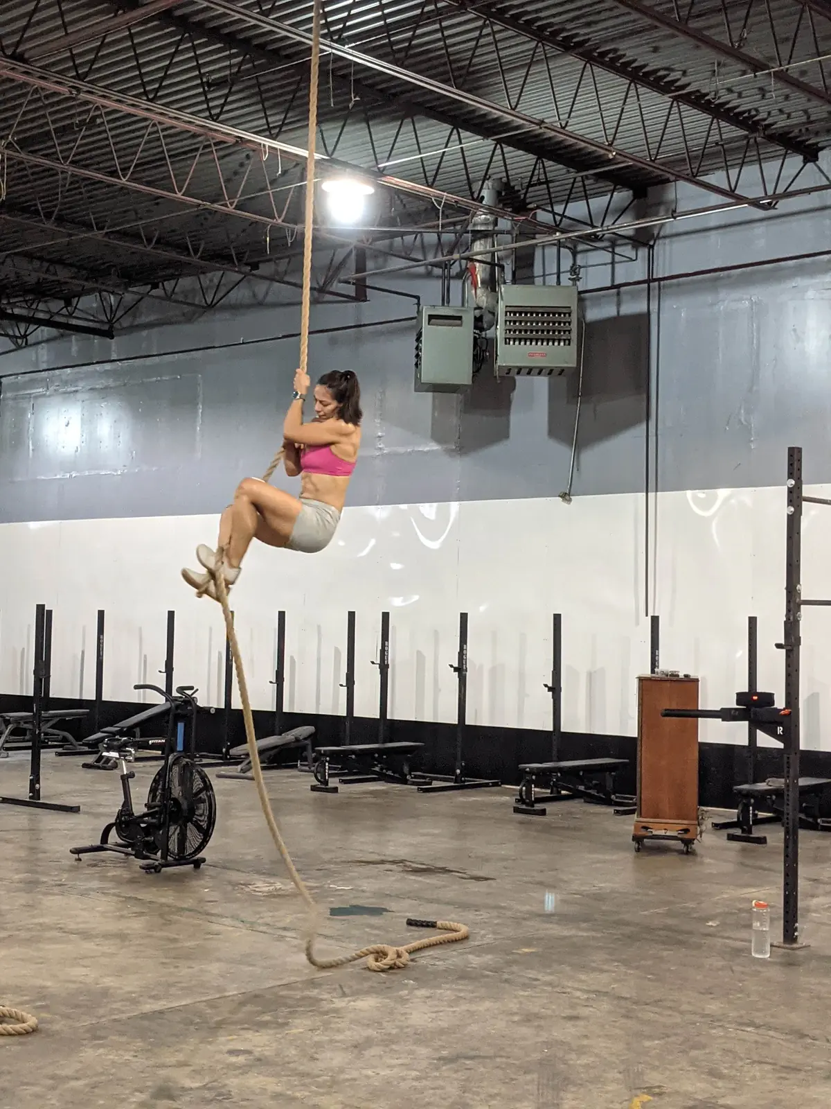 A Fit 901 member climbing high up a gym rope in the warehouse gym.