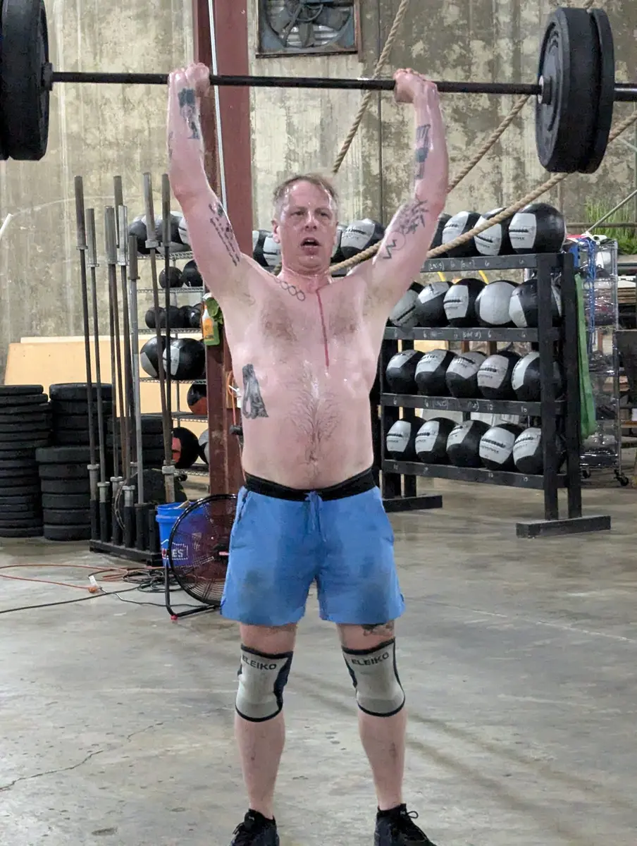 An older Fit 901 member pressing a loaded barbell overhead in the warehouse gym.