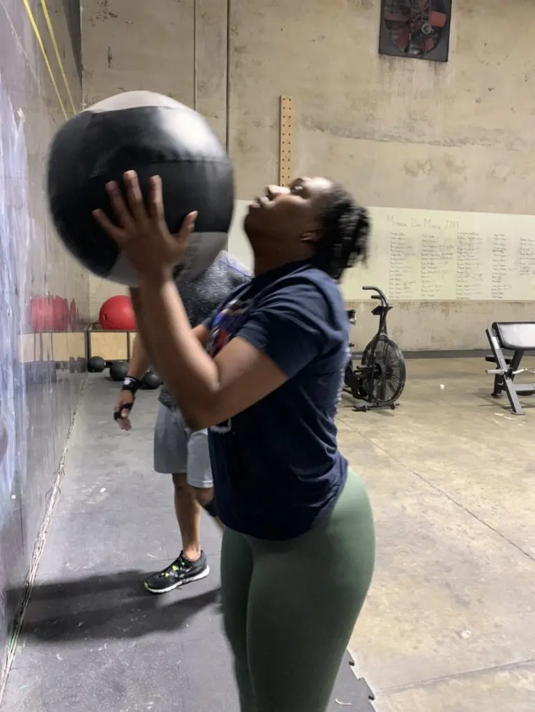 A woman catching a medicine ball against the wall during a workout.