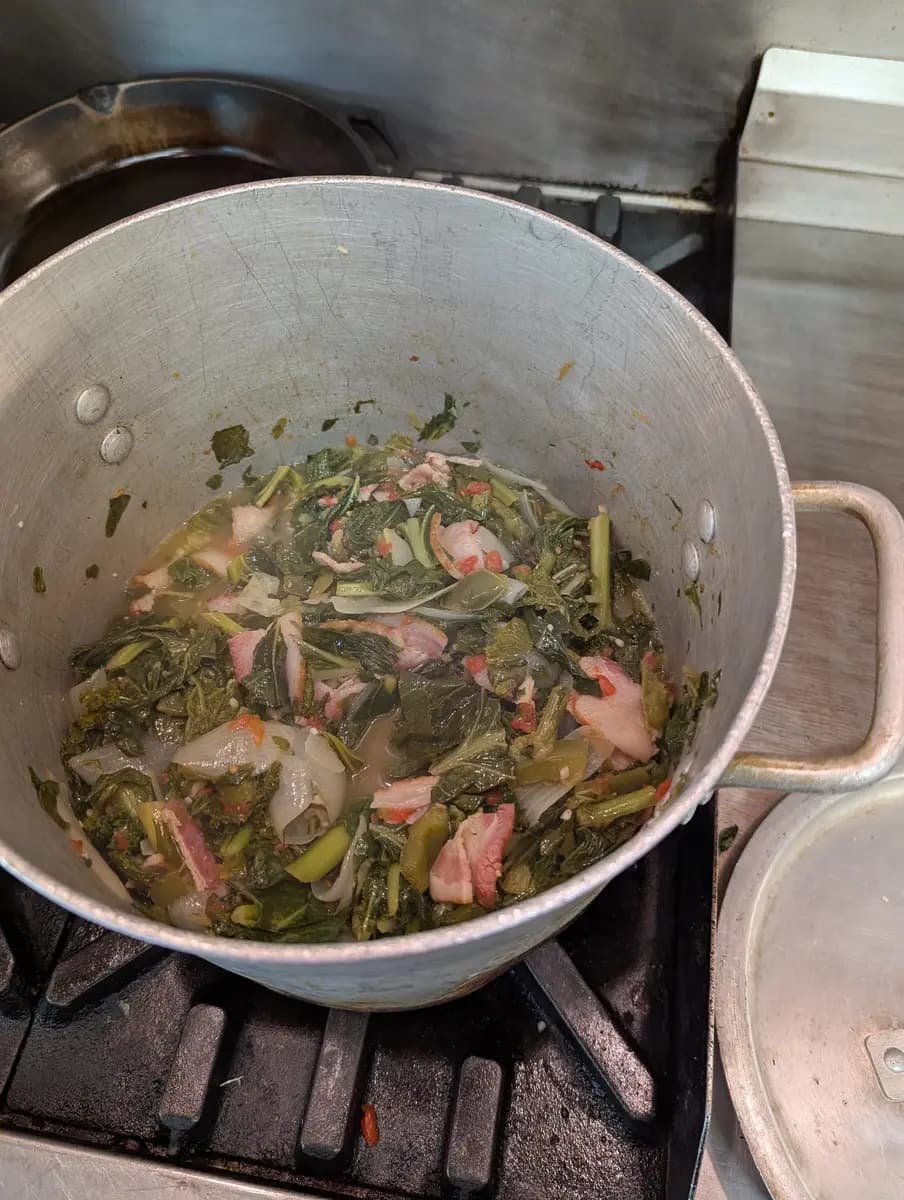 A big pot of collard greens cooking on a home stove.