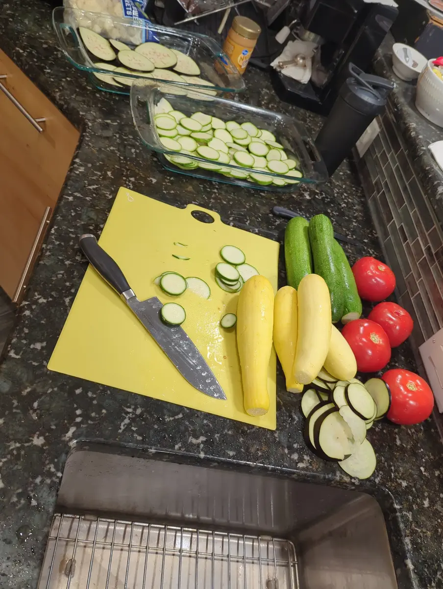 Zucchini, squash and tomatoes being sliced on a cutting board for the week's meals.