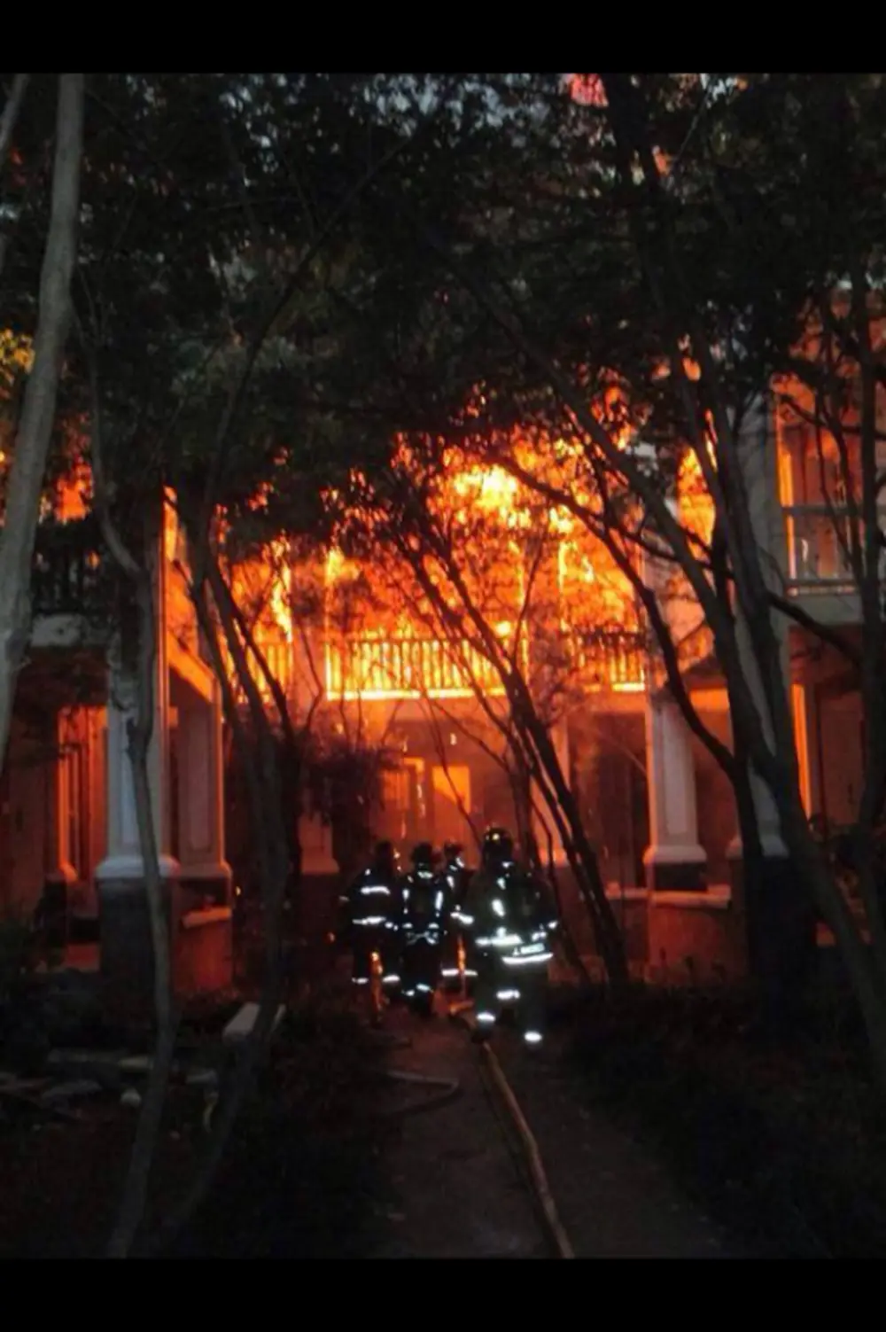 Firefighters advancing a hoseline toward a two-story apartment building fully involved in fire at night.
