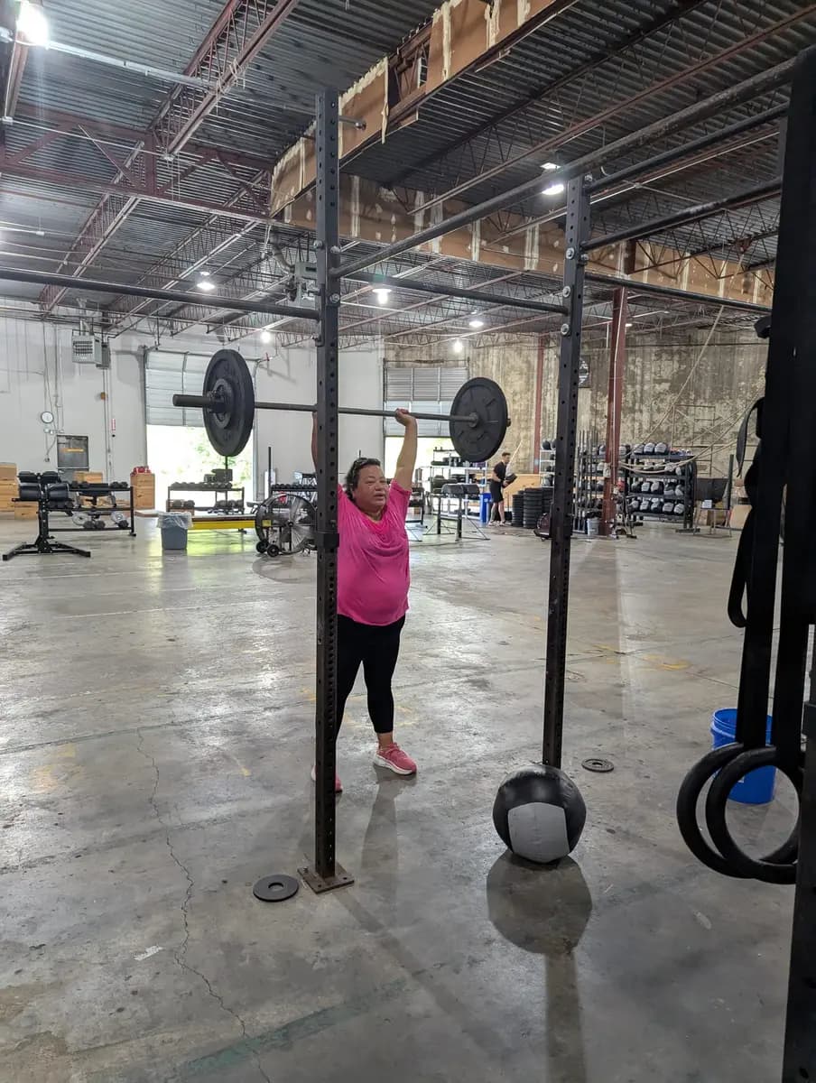 Diana pressing a loaded barbell overhead on the Fit 901 gym floor.